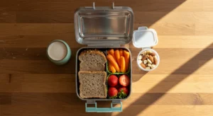 Lancheira escolar aberta contendo frutas frescas, sanduíche natural e recipiente com snacks saudáveis para volta às aulas em agosto, representando alimentação infantil equilibrada